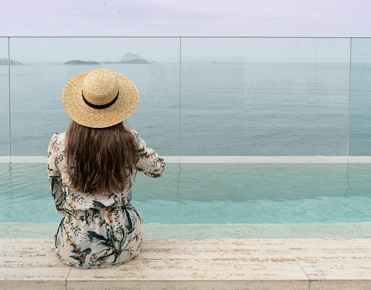 services-img A woman in a floral dress and straw hat enjoys ocean views by an infinity pool.