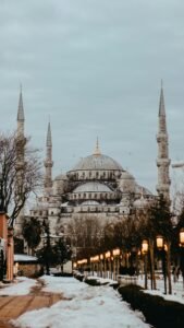 Sultan Ahmed Mosque exterior with towers against snowy walkway and lanterns under cloudy sky in Istanbul Turkey